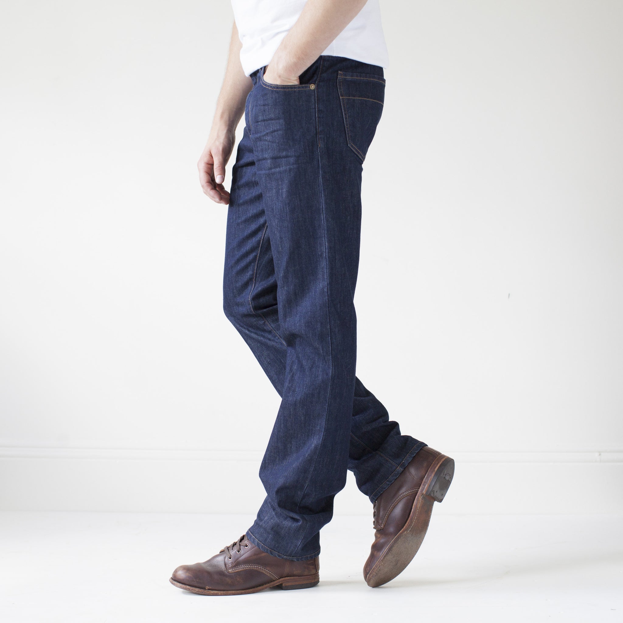angle: resin rinse  A model wears Raleigh Denim Workshop Alexander work fit jeans with a dark wash, side view